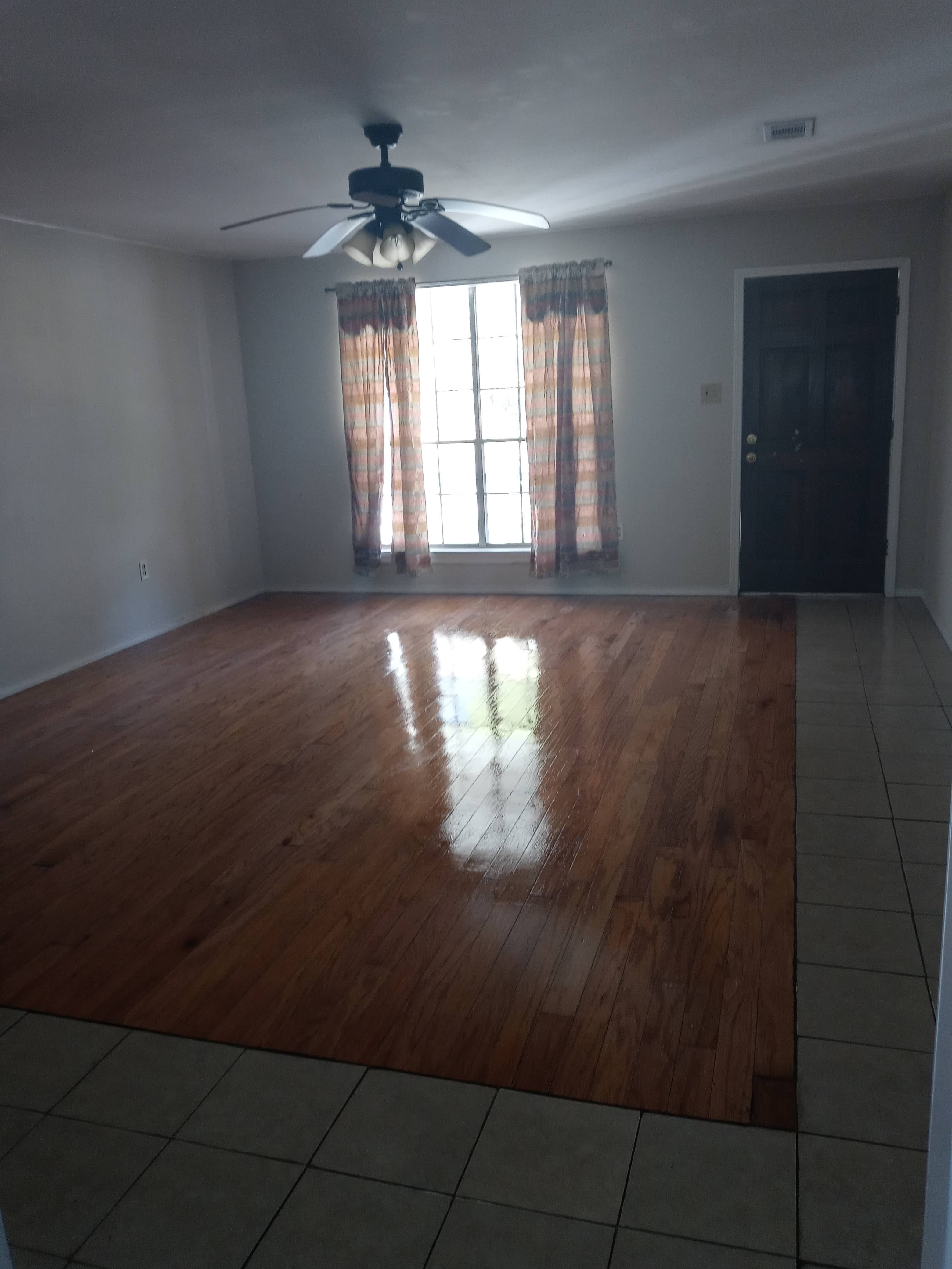 Polished hardwood floors reflecting light in an empty room with a ceiling fan and window.